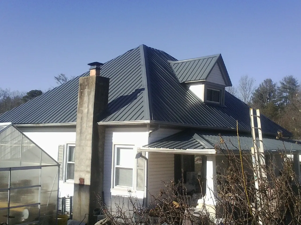 Dark blue standing seam metal roof on a white farmhouse with dormer — Slate & Tile Roof Repair by Roofing Brothers in Clay