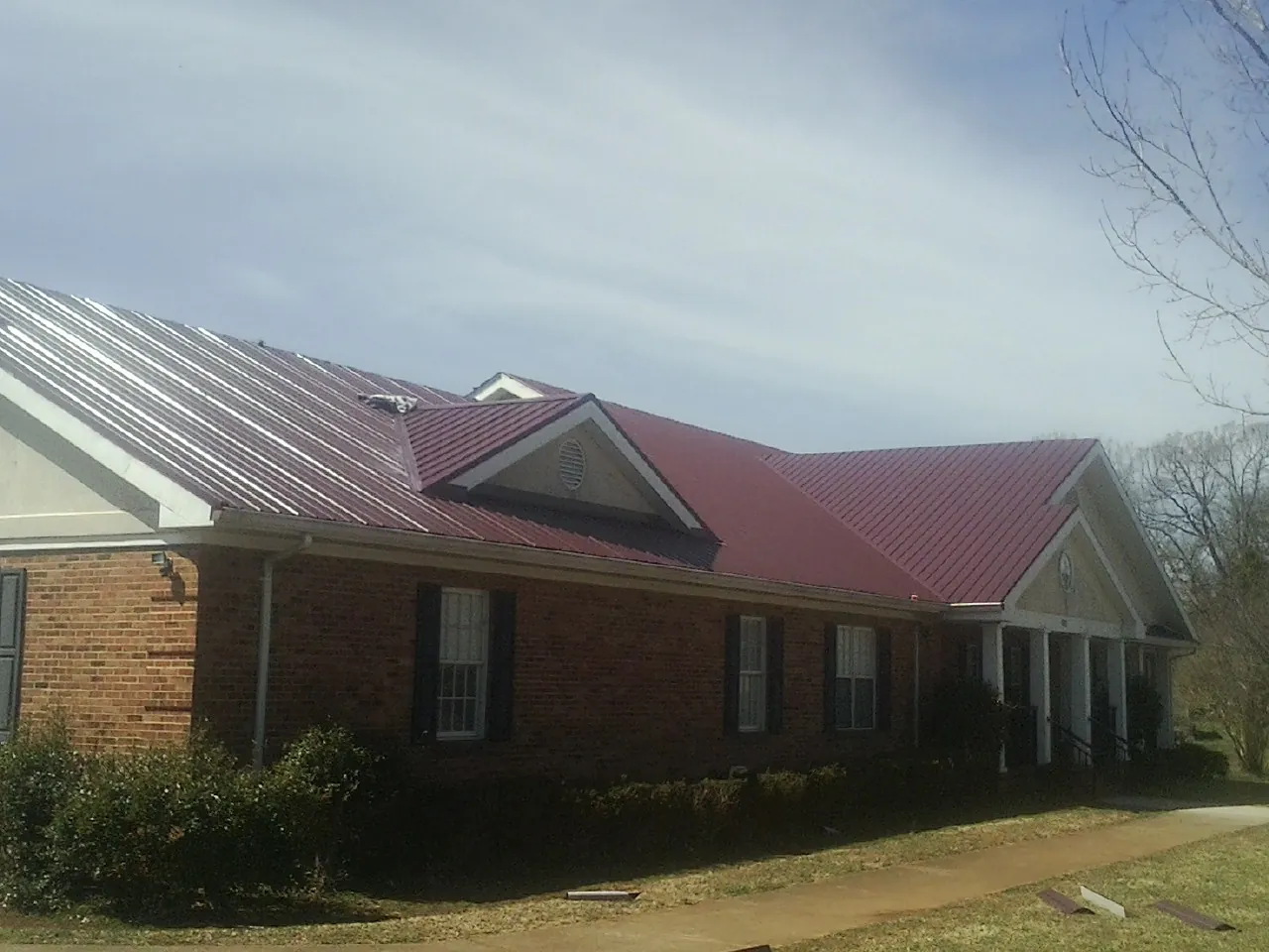 Red metal roof with gabled entries on a long brick building, from a Hail Damage Roof Repair job in Clay