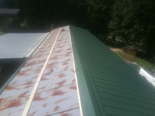 Old rusted panels beside newly installed green metal roofing — Wind Damage Roof Repair by Roofing Brothers in Clay