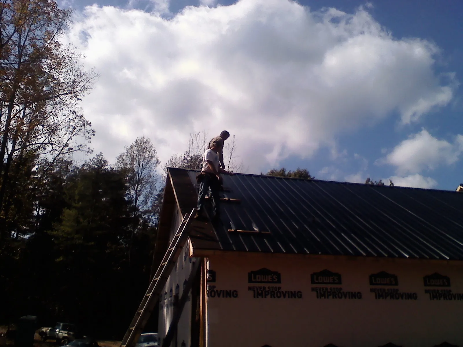 Roofer fastening dark metal panels high against a cloudy sky, from a Roof Inspection job in Clay