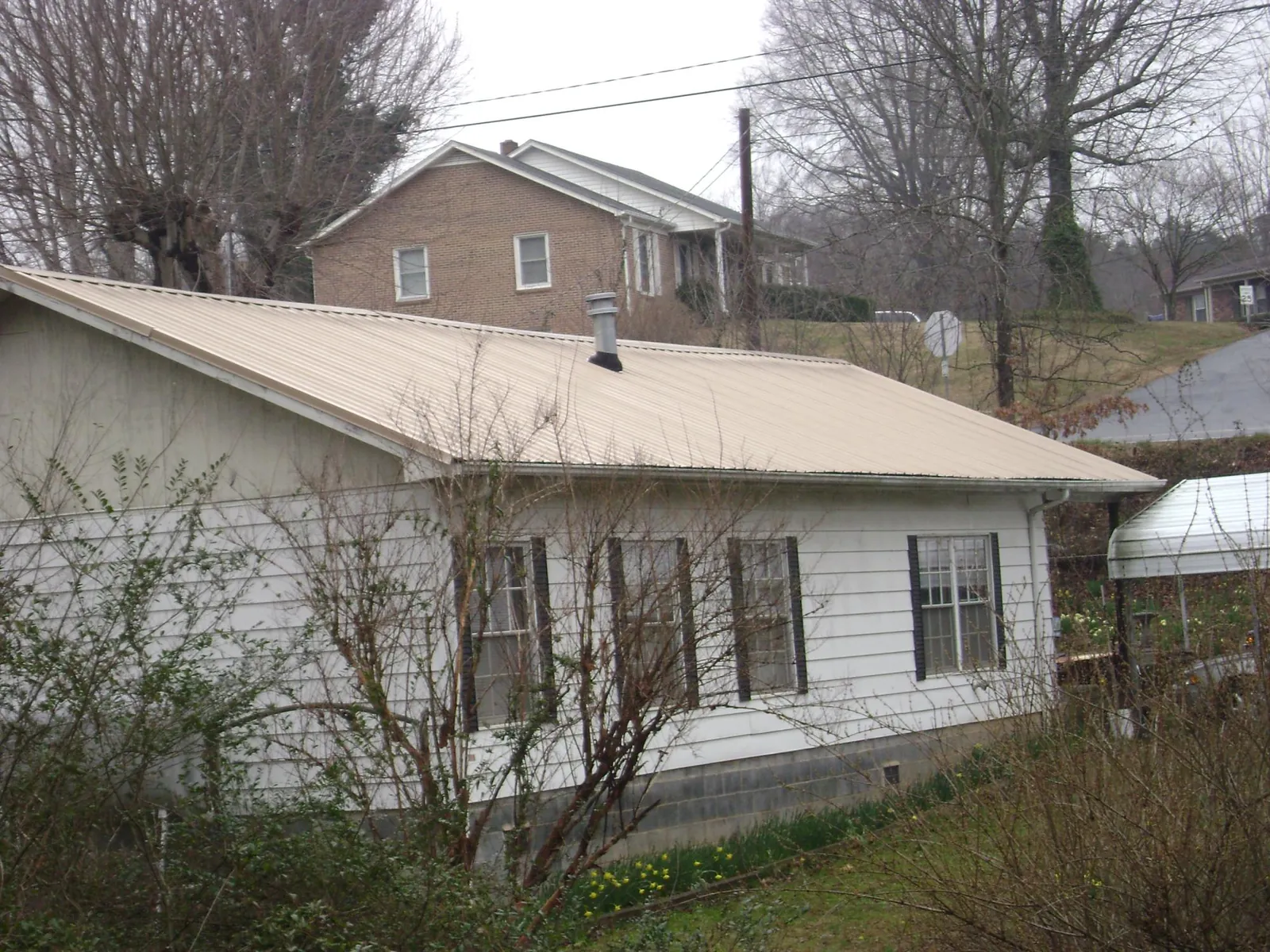 Tan metal roof on a white sided house set into a hillside — Commercial Roofing by Roofing Brothers in Clay
