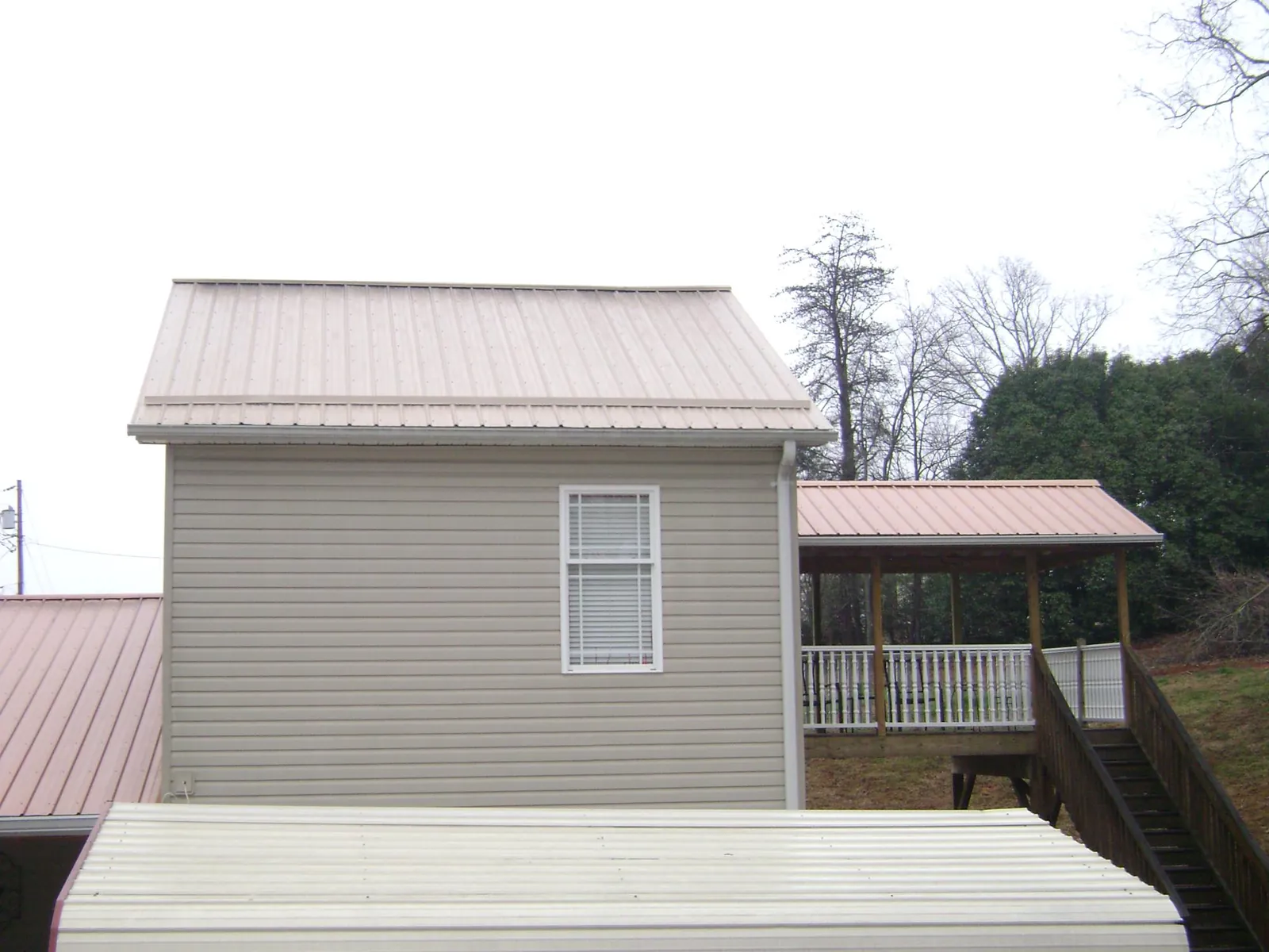 Tan metal roofs on a two story addition and attached porch, from a Roof Replacement job in Clay
